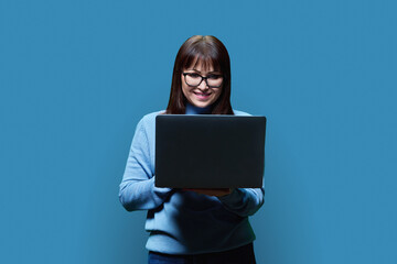 Friendly mature woman using laptop, over blue background