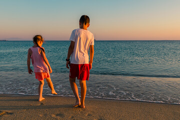 Naxos, Grece - July 20, 2020 - Siblings (girl and boy) having fun at beach during sunset over Naxos...