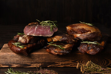 Dried Processed Beef Jerky with herbs and spices on wooden board against black background.