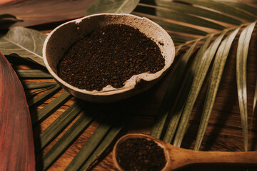 Organic bowl with grounded coffee and wooden spoon on top of green palm leaf 