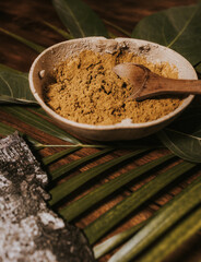Yellow curry powder in organic bowl with wooden spoon surrounded by natural vegetal decoration on a wooden table 
