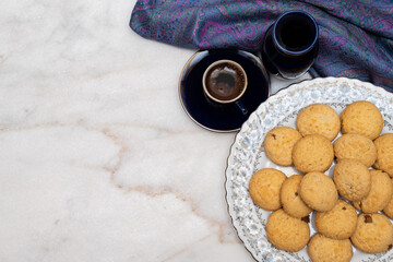 Kahk with sugar sprinkled on top in a rounded china plate and a cup of Turkish coffee on white marble background, (Kahk is a traditional cookies after Ramadan for eid)
