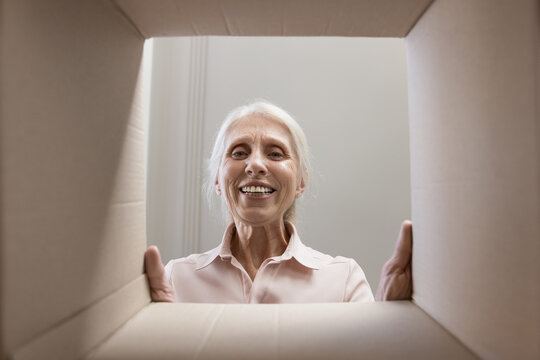 Happy joyful senior woman looking at camera through cardboard box dimensions frame, smiling, laughing. Elder customer lady checking paper container. From inside view portrait