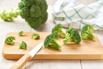 Cooking healthy food, cutting broccoli for baking on a white table.