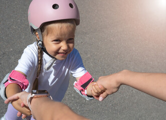 Mother teaching child daughter to skate on inline skates rollers in public park in summer. Family...