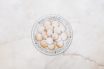 Kahk with sugar sprinkled on top, in a rounded china plate on a white marble background, (Kahk is a traditional cookies after Ramadan for eid)
