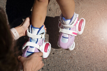 Close-up Mom putting on inline skates rollers to daughter child in public park in summer. Family...