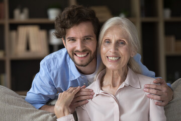 Happy caring handsome grandson guy hugging elder pretty grandma, touching shoulders, looking at...