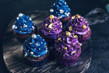 Set of chocolate cupcakes with dark blue and purple cream and golden sprinkles