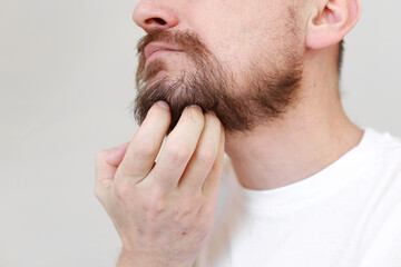 Cropped shot mans hand is unrestrained scratching unshaven chin. Overgrown unkempt male in white t...