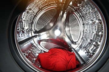 View of the tumble dryer or washing machine drum with red clothes inside. Laundry day. Daily...