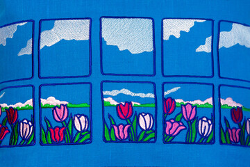 Machine embroidery in the form of tulips on blue linen fabric. Embroidery sample, pattern, image detail on textile.