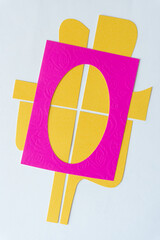 hot pink oval frame on four yellow paper shapes on blank paper