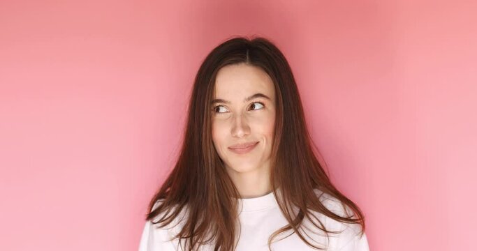 Playful happy flirt brunette woman coquettish look by side, blinking eye, looking at camera with smile, winking and flirting, expressing optimism isolated on pink background.
