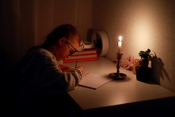 Schoolgirl uses candlelight to writes and reads in darkness without electric lights at home. Teen...