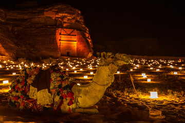 Camel laying in front of ancient tombs of Hegra city illuminated during the night, Al Ula, Saudi Arabia