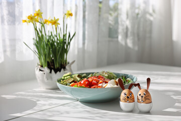 Easter rabbit eggs on white table fresh salad green vegetables yellow flowers sunny day fresh bouquet handmade decorations diy decor copy space Easter concept bunny