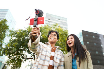 Couple of beautiful Asian influencers using smartphone to streaming live video showing the city and communicate with audience. Online business marketing, tourism, Selling on Social media. . High