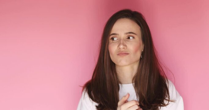 Portrait of nervous woman wringing hands, look by side, search solution of problem. Bed mood. Disappointed troubled confused young woman isolated on pink background.