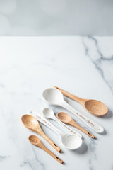 Wooden and ceramic measuring spoons sit on a white marble surface