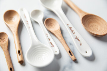 Wooden and ceramic measuring spoons sit on a white marble surface