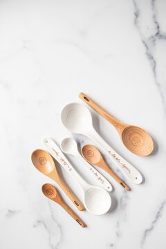 Wooden and ceramic measuring spoons sit on a white marble surface