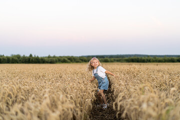 Naklejka na ściany i meble a little blonde curly girl running in a wheat field, the concept of human freedom