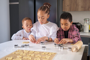 Three cousins cutting cookie shapes in a cookie dough in the kitchen. Horizontal extended family.