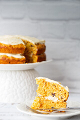 Carrots cake with cream cheese in front of a white brick wall