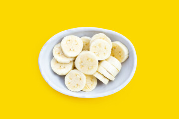 Banana slices in bowl on yellow background.