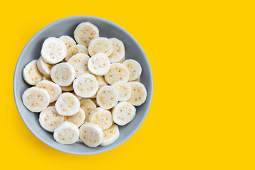 Banana slices in bowl on yellow background.