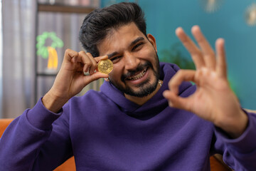 Indian man freelancer holding gold coin successful developer programmer. Ok. Hindu guy stock trader...
