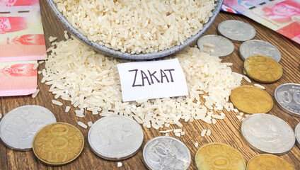 Zakat Islamic Concept. “ZAKAT” wordings, rice, coins, and Indonesian rupiah banknotes on wooden background
