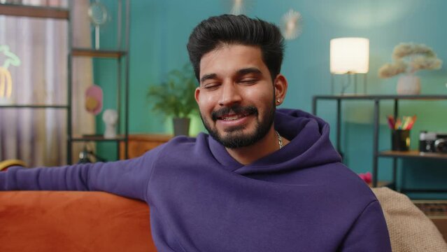 Portrait of happy calm indian man at home couch smiling friendly, glad expression looking away dreaming resting, relaxation feel satisfied concept good news, celebrate win. Hindu guy in living room