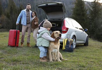 Dog, cute little girl and her parents near car in mountains. Family traveling with pet
