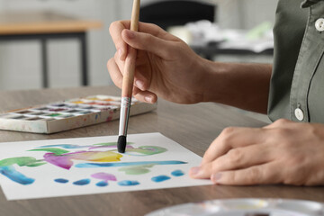 Obraz premium Woman painting with watercolor at wooden table indoors, closeup