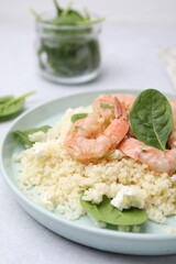 Plate of delicious couscous with shrimps and spinach on white table, closeup