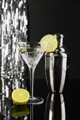 Martini cocktail with lemon slice and shaker on black and silver background