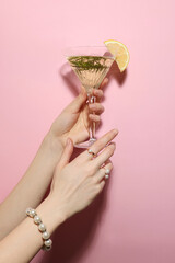 Woman holding martini glass of refreshing cocktail with lemon slice and rosemary on pink background, closeup