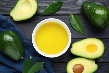 Bowl with oil, ripe fresh avocados and leaves on black wooden table, flat lay