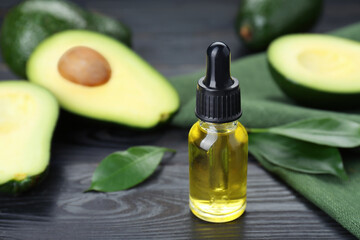 Bottle with essential oil and ripe fresh avocados on black wooden table, closeup