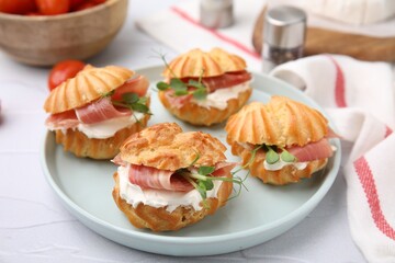 Delicious profiteroles with cream cheese and prosciutto on white table, closeup