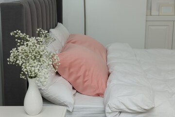 Obraz na płótnie Canvas Vase with beautiful flowers on white bedside table and comfortable bed in room. Stylish interior