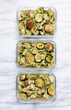 Pasta salad in meal prep containers with bowtie pasta, zucchini, cheese and pesto