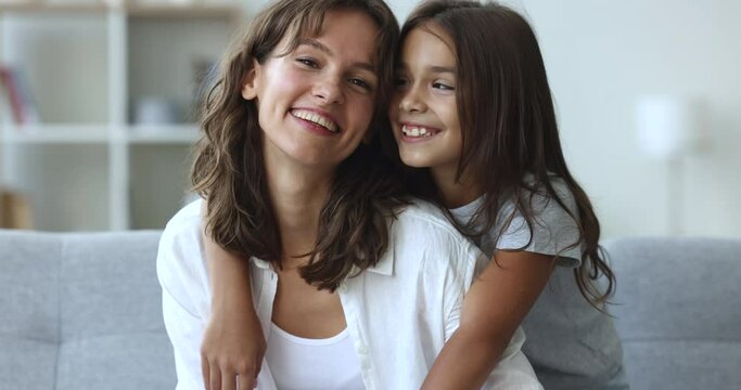 Happy cheerful woman plays, pose for cam with little 10s daughter, sit on couch staring at camera, tickling laughing feel overjoyed, close up. Motherhood, priceless time, unconditional love, childhood