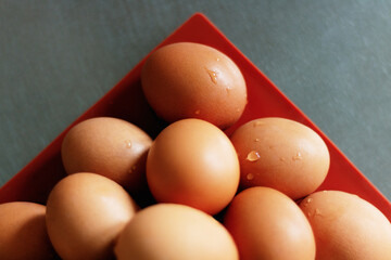 Eggs stacked in the corner of a red tray on silver aluminum surface in top view.