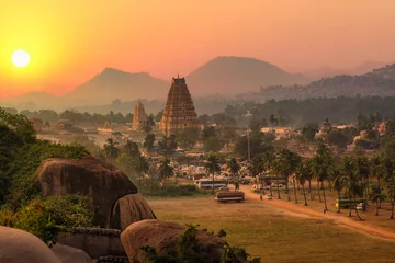 Vlies Fototapete Altes Gebäude Virupaksha temple with scenic Hampi landscape and cityscape at sunset at Karnataka India