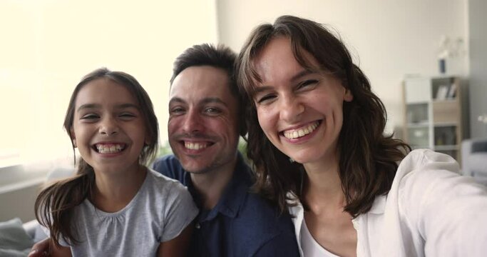 Close up webcam view happy Hispanic couple and little cute daughter making funny faces, grimacing pose in front of smartphone camera, spend leisure use modern tech, new apps, make selfie, having fun