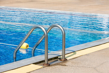 Ladder stainless handrails for descent into swimming pool. Swimming pool with handrail . Ladder of a swimming pool. Horizontal shot. stairs swimming pool. Stainless steel ladder