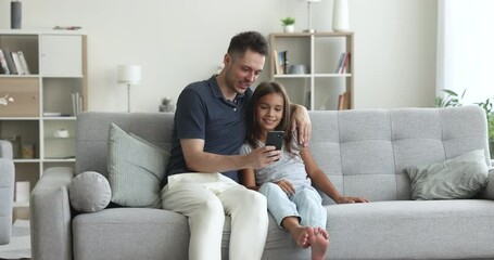 Loving dad teach, explain, show to daughter new mobile app, spend time together with cool, amusing application sit on sofa look at smartphone screen. Young generation use modern gadget, internet usage - Powered by Adobe